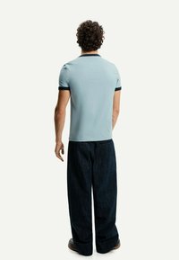 Light blue polo shirt with navy collar and sleeve accents, paired with wide dark denim trousers. Visible back design and fitted style.