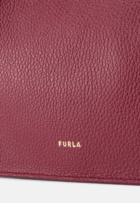 Bordeaux læderpunge med en tekstureret overflade. Har et guldfolieret "FURLA" logo på bunden, der fremhæver det kompakte design.