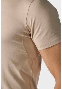 Beżowa koszulka z krótkim rękawem wykonana z gładkiego materiału, z płaskimi szwami i dopasowanym krojem. Detale bocznych paneli wyostrzają sylwetkę.