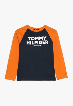 Granatowa koszula z długim rękawem, pomarańczowymi rękawami raglanowymi i białym napisem "Tommy Hilfiger New York 1985" z przodu.