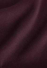 Krupan plan meke, rebraste tamnoljubičaste tkanine s blagim naborima i vidljivim teksturiranim okomitim linijama na površini.