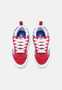 Sneaker rosse e bianche con un accento a scacchi blu, dotate di una tomaia in suede testurizzato, lacci bianchi e un passante sul tallone.