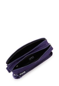 Bandolera Kipling morada con dos compartimentos abiertos con cremallera y un pequeño llavero esponjoso sobre fondo blanco.