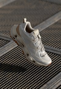 Light beige sneaker with textured mesh and synthetic panels. Features a thick, cushioned sole and tonal laces. Brand logo visible on side.