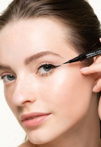 L'eyeliner liquido nero con punta di precisione viene applicato sulla palpebra superiore. Il modello ha la pelle liscia e lentiggini chiare.