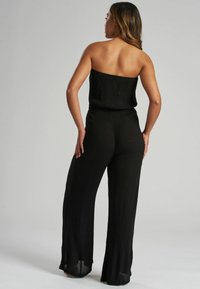 Mono negro sin tirantes con perneras anchas, hecho de una tela ligera y texturizada. Presenta una cinturilla elástica para un mejor ajuste.