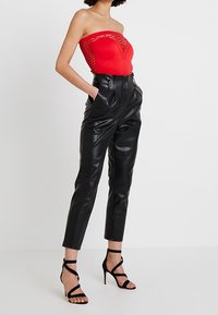 Rode strapless jumpsuit met kantdetailing, gecombineerd met hoge zwarte neplederen broeken en zwarte sandalen met bandjes.