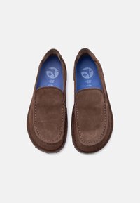 Ζευγάρι καφέ σουέντ μοκασίνια χωρίς κορδόνια με μπλε μαλακές εσωτερικές σόλες, τοποθετημένα δίπλα δίπλα σε λευκό φόντο.