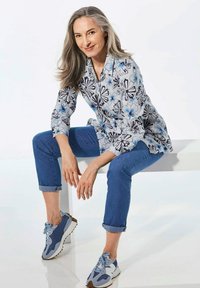 Bluse mit floralen Mustern in Hellblau und Schwarz, kombiniert mit hochgekrempelten blauen Jeans und blauen Sportschuhen mit braunen Sohlen.