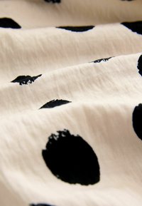 Il tessuto di cotone con una superficie testurizzata presenta grandi pois neri su uno sfondo crema, creando un contrasto di colori e motivi.