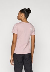 Φωτεινό ροζ βαμβακερό t-shirt με κοντά μανίκια, στρογγυλή λαιμόκοψη και λευκό λογότυπο στο πάνω μέρος της πλάτης. Συνδυάζεται με μαύρο παντελόνι.