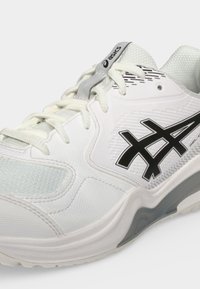 Άσπρο αθλητικό παπούτσι ASICS με μαύρο λογότυπο, ύφασμα από δίχτυ, λευκά κορδόνια και γκρι λεπτομέρειες στη σόλα και τη γλώσσα.