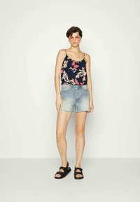 Top de tanque azul marinho com padrão floral e alças finas, combinado com calções de ganga azul claros. Sandálias pretas completam o visual.