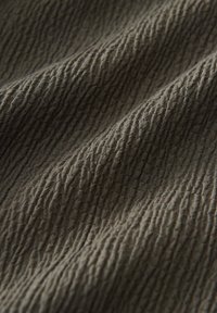 Gros plan d'un tissu froissé et texturé de couleur vert olive atténué avec un motif linéaire doux et irrégulier et des plis visibles.