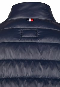 Marineblaue isolierte Jacke mit strukturiertem Finish, ausgestattet mit einem hohen Kragen und einem kleinen dreifarbigen Akzent am Hals.