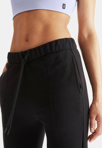 Black sweatpants with a drawstring waist, featuring side pockets, smooth texture, and stitching details for a fitted athletic look.