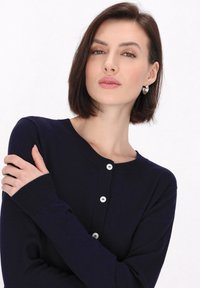 Námornícky cardigan vyrobený z mäkkej tkaniny, s okrúhlym výstrihom, dlhými rukávmi a piatimi bielymi gombíkmi na prednej strane. Texturované rebrované manžety.