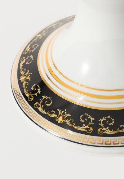 Λευκό φλιτζάνι τσαγιού σε μαύρο πιατάκι με χρυσά διακοσμητικά μοτίβα λουλουδιών και γεωμετρικά κατά μήκος της άκρης.