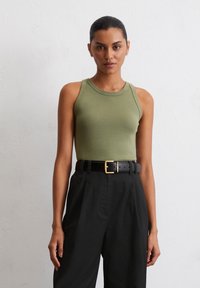 Débardeur ajusté vert olive avec encolure ronde, associé à un pantalon noir taille haute et une ceinture noire avec une boucle en or.