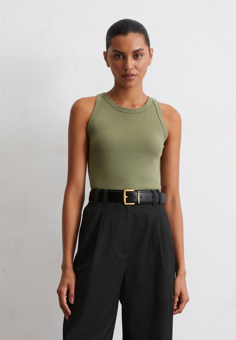 Débardeur ajusté vert olive avec encolure ronde, associé à un pantalon noir taille haute et une ceinture noire avec une boucle en or.