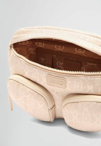 Trousse de maquillage beige clair avec un motif texturé, poches zippées doubles et une étiquette de logo à l'intérieur. Doublure en tissu doux avec un branding subtil.