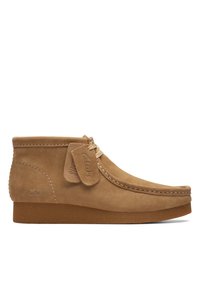 Botas tobilleras de ante en color beige con un diseño cosido, cordones a juego y una etiqueta de marca. Suela de goma texturizada que proporciona agarre y estabilidad.