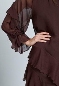 Braune Chiffonbluse mit Rüschensleeves und einem mehrschichtigen Design, das sanft geraffte Details und eine weiche Textur aufweist.