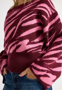 Maglione in misto lana con un audace motivo astratto rosa e bordeaux, bordi a coste e una vestibilità rilassata. Il tessuto ha una superficie morbida e strutturata.