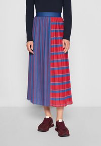 Plisserad midikjol med en design i hälften röd och hälften blå med vertikala och horisontella ränder. I kombination med mörka sneakers.