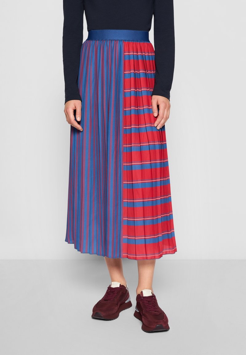 Plisserad midikjol med en design i hälften röd och hälften blå med vertikala och horisontella ränder. I kombination med mörka sneakers.