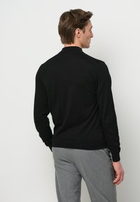 Svart stickad tröja med rund krage, ribbade ärmslut och nederkant. Tyget verkar glatt och framhäver en klassisk, figurnära siluett.