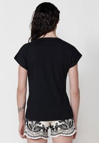 Camiseta negra de manga corta hecha de algodón, diseño ajustado, combinada con pantalones cortos blancos texturizados que presentan bordados florales negros y flecos.