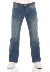 Jeans de mezclilla azul con un corte relajado, que presentan un lavado desgastado, cinco bolsillos, herrajes de metal y trabillas para el cinturón. Combinados con zapatillas blancas.