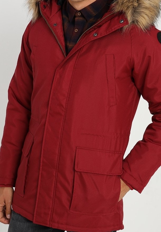 Chaqueta parka aislada roja con capucha de piel sintética, que cuenta con dos bolsillos delanteros y cierre de cremallera. Tela texturizada con acabado mate.