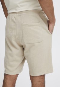 Shorts en coton beige avec un tissu texturé, une ceinture élastique et une poche arrière unique. Revers ourlés à mi-cuisse.