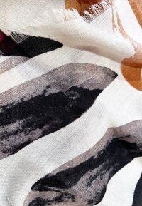 Tessuto con una texture morbida che presenta motivi astratti in tonalità terrose di nero, marrone e bianco, con bordi sfilacciati.