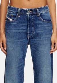 Jeans in denim blu con un design a gamba dritta, vita alta, tasche frontali e distintive cuciture a contrasto. Tessuto liscio e lavaggio classico.