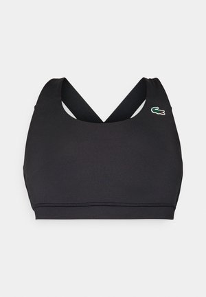 Sujetador deportivo negro con escote redondeado, tirantes en forma de cruz y un pequeño logo de Lacoste en verde, rojo y blanco. Textura de tela suave.