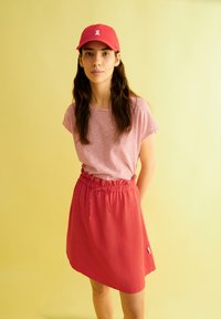 Red cap with logo, striped short-sleeve shirt, and a knee-length red skirt with an elastic waistband and drawstring details. Yellow background.