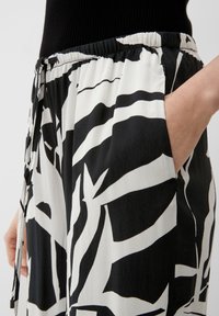 Pantalon à motifs noir et blanc avec une taille élastique, un cordon de serrage et des poches latérales, fabriqué dans un tissu léger et lisse.