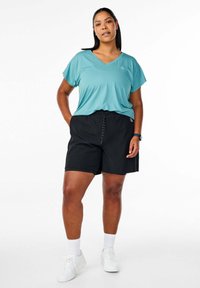 Vaalean turkoosi V-pääntie t-paita lyhyillä hihoilla, yhdistettynä mustiin shortseihin, joissa on joustava vyötärö, ja valkoisiin urheilujalkineisiin. Rentoa ja mukavaa istuvuutta.