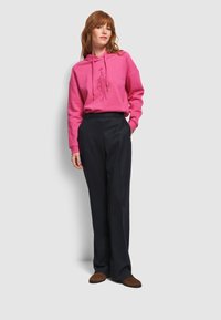 Różowa bluza z kapturem ze sznurkiem oraz grafiką z przodu, w zestawieniu z czarnymi spodniami w prążki i brązowymi, wzorzystymi mokasynami.