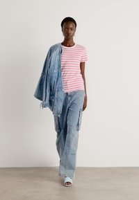 Lys rosa og hvit stripete t-skjorte sammen med en lys blå denimjakke og cargo-bukser. Modellen har på seg åpne, hvite hæler.
