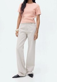 Haut rose texturé à manches courtes associé à un pantalon large beige clair et des chaussures noires à bouts pointus. Tissu lisse et design minimaliste.