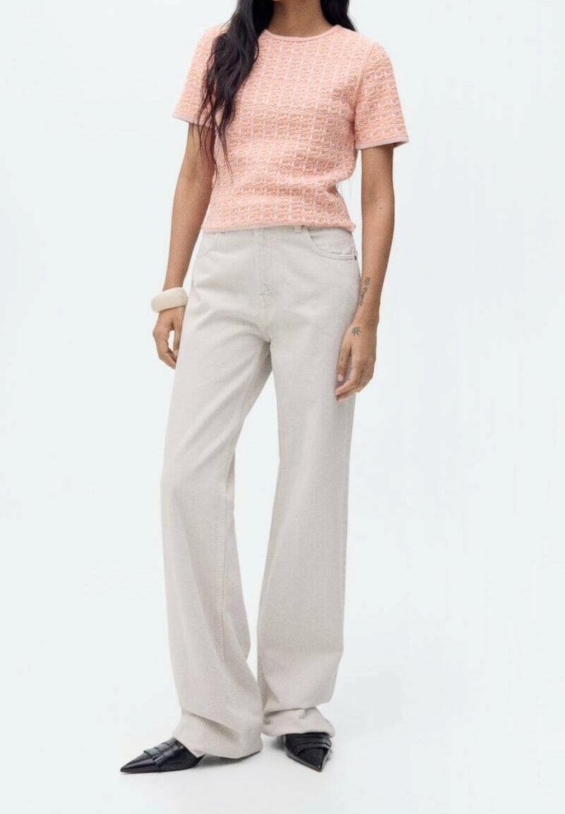 Haut rose texturé à manches courtes associé à un pantalon large beige clair et des chaussures noires à bouts pointus. Tissu lisse et design minimaliste.