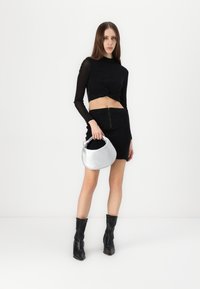 Crni crop top s dugim rukavima, crna suknja s patentnim zatvaračem, srebrna hobo torba i crne čizme do koljena. Glatke teksture i usklađen dizajn.