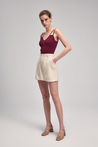 Burgundy ribbattuok, jossa on ohuet olkaimet, yhdistettynä kermaisiin korkeavyötäröisiin shortseihin ja beigeihin korkokengiin koristeellisilla yksityiskohdilla.