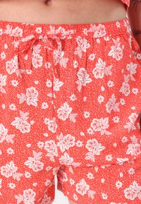 Røde blomstrete shortser med et hvitt blomsterdesign og små prikker. Laget av lett materiale, med elastisk midje og snøring.