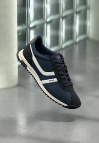 Navy blue sneaker with white side stripes, rounded toe, textured upper, and rubber sole. "BOSS" logo on tongue and side.
