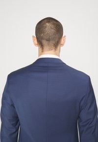 Navy blue suit jacket with a tailored fit and single vent at the back. Smooth fabric texture with structured shoulders and lapels.